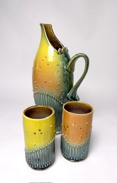 A pitcher and two tumblers by Michael Lemke, glazed in yellow, orange and teal Ware glazes over carved texture