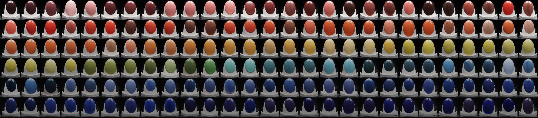 A long row of Ware ceramic glazes fired on test forms, running from reds and oranges through yellows and greens to deep blues