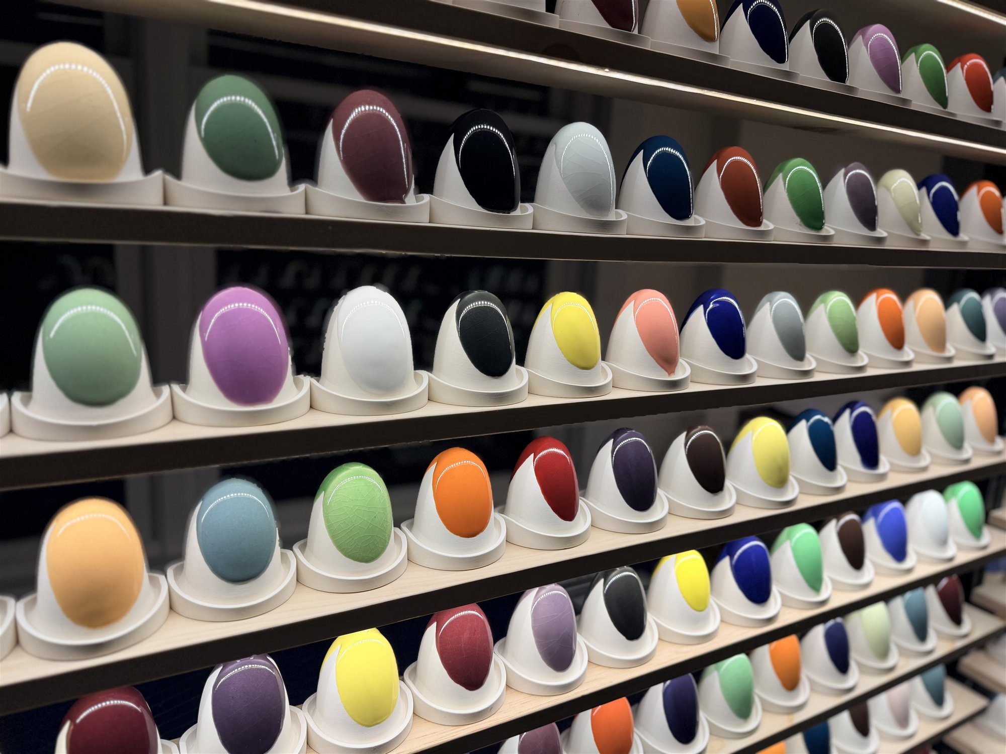 Shelves of fired glaze test specimens in the Ceramic Materials Workshop glaze library, lit and sorted by color